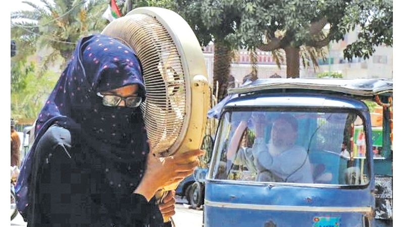 A woman carries a pedestal fan for repair due to the hot and humid weather in Karachi.