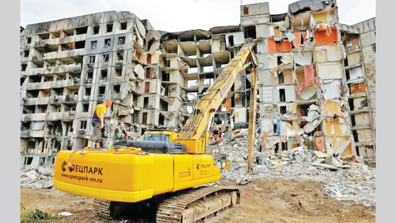 A worker stands on an excavator in front of a destroyed apartment building in Mariupol.