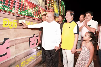 Speaker Mahinda Yapa Abeywardena inaugurating the lighting system at the Homagama Dharma Rashmi Poson Zone pandol yesterday. Transport, Highways and Mass Media Minister Dr. Bandula Gunawardhana looks on.